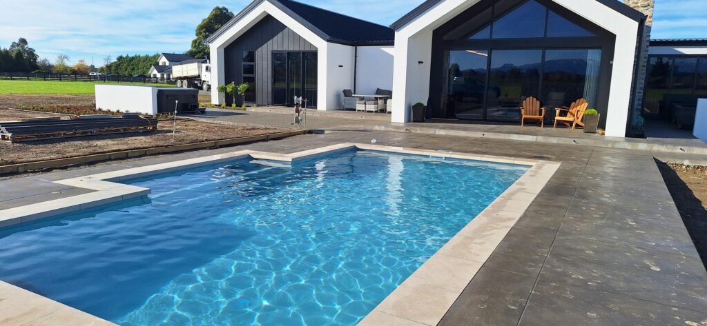 Modern Bermuda pool with sleek design, surrounded by a spacious outdoor patio, perfect for relaxation and entertaining. Custom-built inground pool featuring contemporary finishes and scenic views.