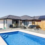 Bright blue modern swimming pool with clear water, surrounded by a stylish wooden deck and outdoor lounge furniture, ideal for Bermuda pool installations and backyard leisure.
