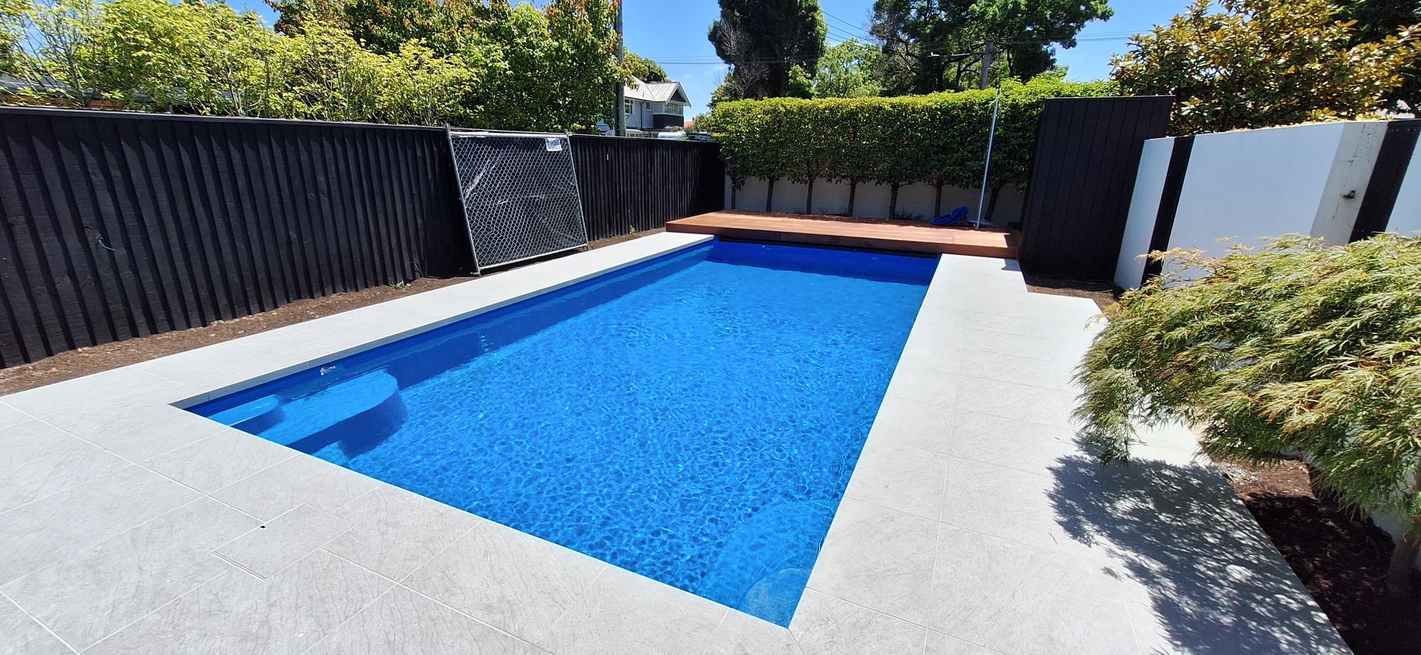 Sleek modern swimming pool with blue water, surrounded by white tiling, black fencing, and lush greenery in Bermuda, perfect for luxury outdoor living and pool installation services.