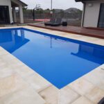 Modern in-ground swimming pool with clear blue water, surrounded by beige natural stone decking, perfect for Bermuda outdoor living.