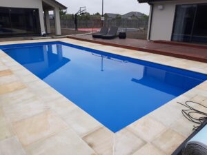 Modern in-ground swimming pool with clear blue water, surrounded by beige natural stone decking, perfect for Bermuda outdoor living.
