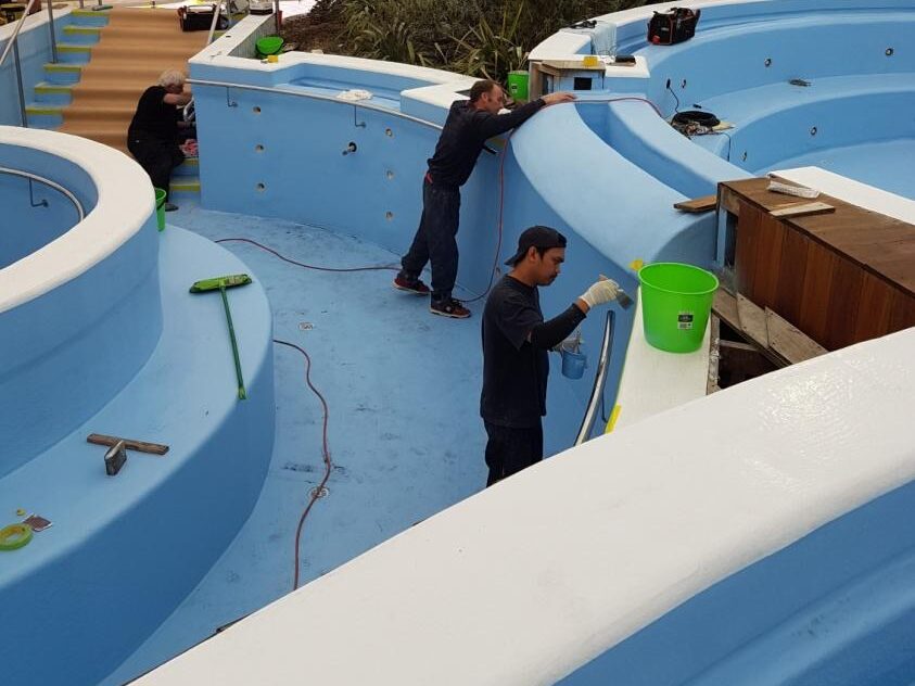 Blue in-ground pool under construction with workers applying finishing touches of a fibreglass pool lining