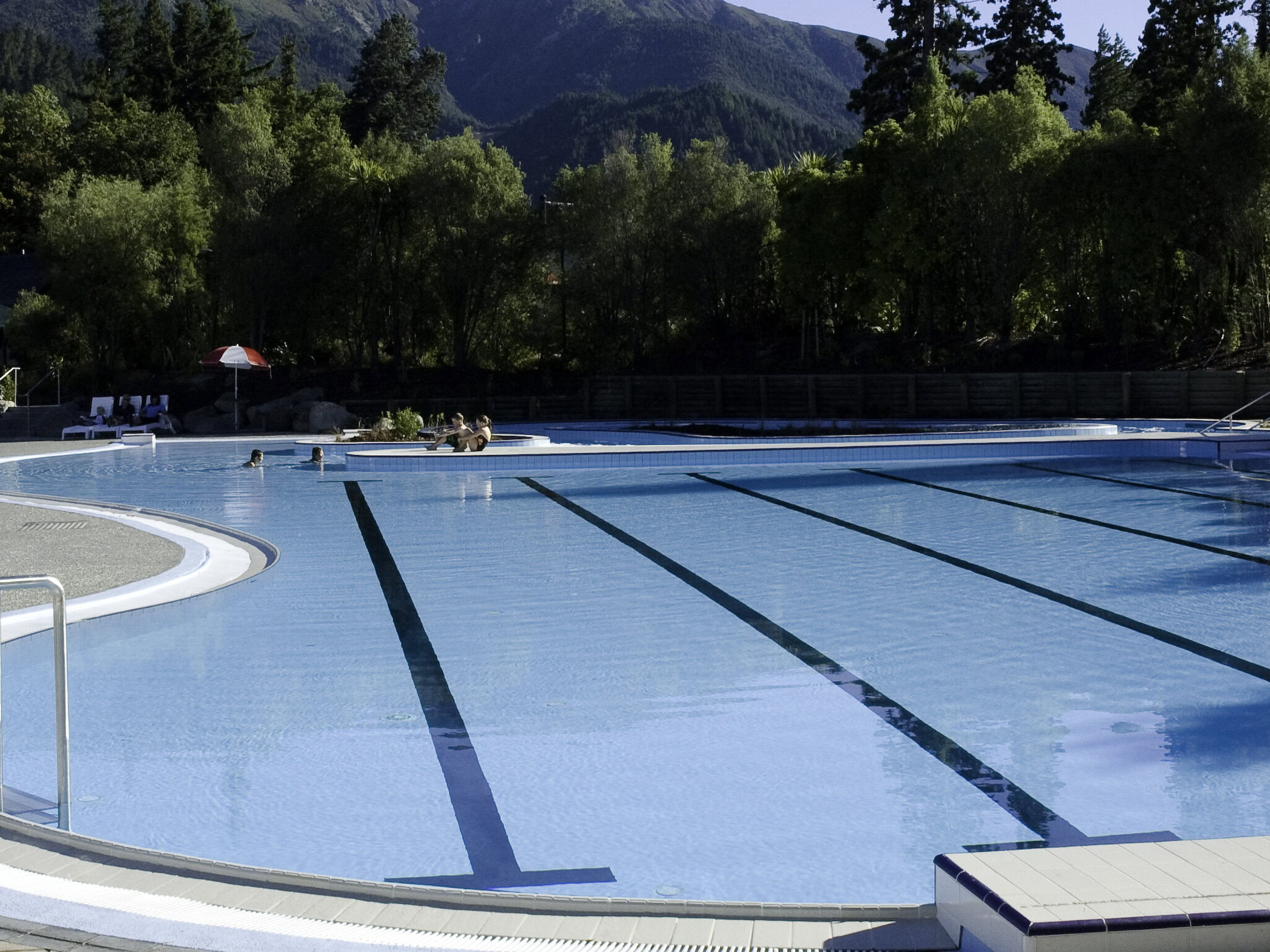 Hanmer outdoor pool with fibreglass pool lining, featuring a modern design, clear blue water, and poolside seating, perfect for relaxation and recreation in a tropical setting.