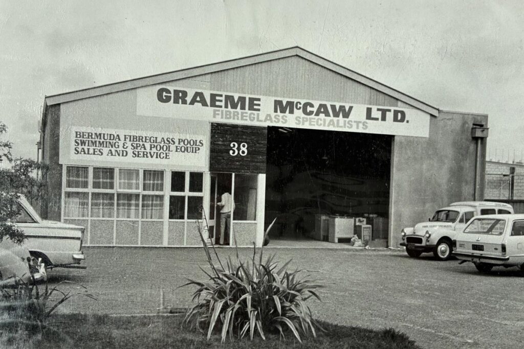 Vintage Bermuda Pools fibreglass shop exterior in black and white, showcasing the garage-style entrance and classic cars, highlighting Bermuda fibreglass pools, swimming, spa pool equipment, and sales service.