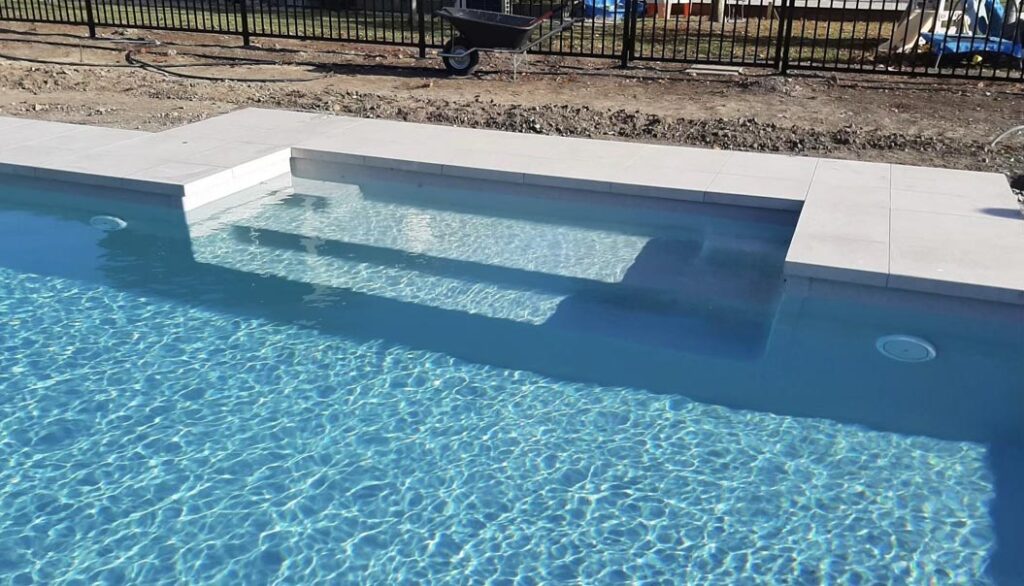 Custom-built swimming pool with integrated steps and clear blue water, perfect for relaxation and leisure. High-quality Bermuda Pools installation showcasing modern design in New Zealand.