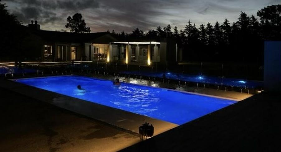 Luxurious illuminated outdoor swimming pool at night with vibrant blue water, modern design, and warm ambient lighting, perfect for relaxation and entertainment in Bermuda.