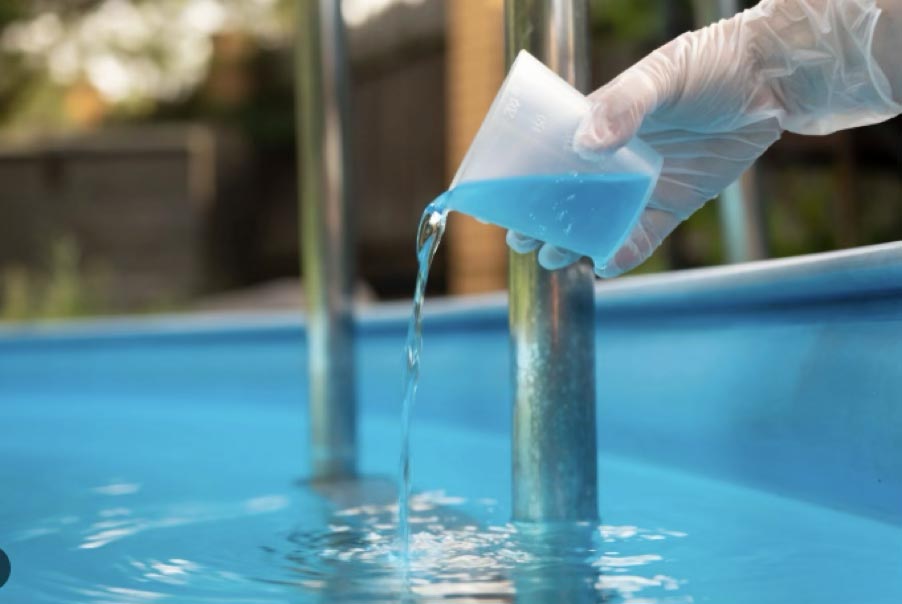 Test tube with blue chemical being poured into Bermuda pool for water treatment, focusing on pool maintenance and water quality.